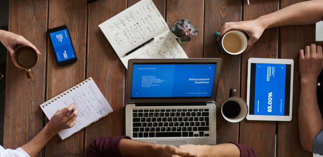 In the image, you can see a table with three electronic devices on it: a cell phone, a tablet, and a laptop. These devices are synchronized and display relevant information about customer and business management. The screens have minimal text, with a blue background and white writing. In addition to the electronics, there are three cups holding coffee and tea. This illustrates the calm and light routine in managing the business.